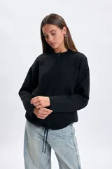 Campera de punto color negro con cierre frontal, cuello redondo y mangas largas. Presenta un diseño minimalista y versátil con cordones ajustables en la parte inferior.