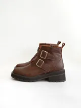 Botas cortas de cuero color marrón con suela track negra. Presentan dos correas ajustables con hebillas metálicas plateadas en el empeine y cierre lateral interno.