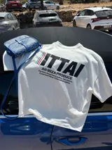 Remera marrón de corte holgado con estampado en la espalda que incluye la palabra "ITTAI" en blanco con líneas rojas y azules, la frase "AN IBIZA PRODUCE" y un texto más pequeño que dice "Ittai Stars Department Gallery - Ibiza Edition. If you're in Ibiza, 112 is not an option.".