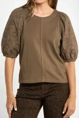 Remera de algodón color rosado con mangas cortas abullonadas de broderie con diseño floral calado. Presenta cuello redondo y costura vertical central en el frente.