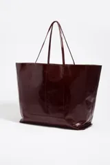 Bolso shopper grande Bimba Y Lola confeccionado en cuero vacuno con acabado brillante en color bordó. Cuenta con estructura blanda, doble asa fina de hombro y detalle de logo metálico en la parte inferior.