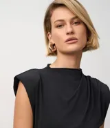 Vestido midi negro sin mangas, con cuello alto y sisa amplia. Presenta fruncidos delanteros que crean un efecto drapeado en la falda.