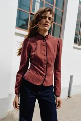 Blazer de terciopelo con cuello subido y manga larga. Presenta cierre frontal con botones, bolsillos de vivo en el delantero y detalle de vivo a contraste en los bordes.