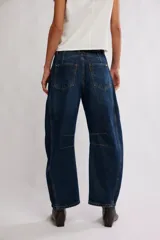 Jean de denim azul con silueta barrel y tiro medio, piernas amplias que se afinan en los tobillos, desgastes sutiles y costuras en las piernas.