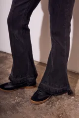 Pantalón de jean negro con corte flare, tiro medio y ruedo desflecado.