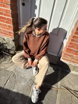 Buzo marrón de algodón, corte holgado, con cuello redondo y puños ajustados.