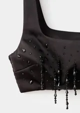 Top corto de satén negro con escote cuadrado y tirantes anchos. Presenta un diseño crop con abalorios colgantes de cristal en el ruedo y panel elástico en la espalda.