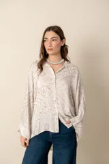 Camisa blanca con estampado de diseño bandana en tonos beige, de corte amplio, con cuello camisero y cierre frontal con botones.