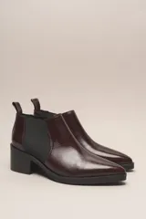 Botín chelsea de cuero vacuno color bordó con acabado charol, punta fina y elástico lateral negro. Posee un taco ancho y bajo de goma.