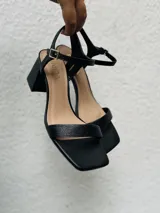 Sandalias negras de tacón bajo y ancho, con punta cuadrada, talón abierto y tira fina ajustable al tobillo.
