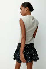 Pollera mini de satén negro con estampado de lunares blancos. Presenta una cintura ancha con pliegues horizontales y un diseño escalonado con volados que aportan volumen y movimiento.