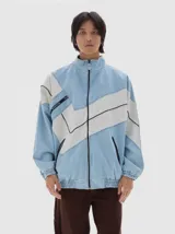 Campera de denim estilo deportivo con diseño de paneles en tonos azul claro y blanco, cuello alto, cierre frontal y bolsillos laterales con cierre. Presenta corte oversized con puños y cintura elásticos.