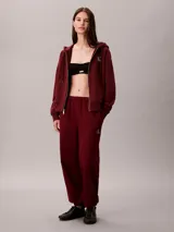 Jogger de felpa color bordó, de corte tapered y tiro medio, con cintura elástica y bolsillos laterales. Cuenta con puños ajustados en los tobillos y detalle del monograma de Calvin Klein en la pierna.