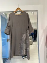 Vestido midi de lino color visón, con cuello redondo, mangas tres cuartos y diseño asimétrico con botones decorativos y estampado floral en la parte inferior.