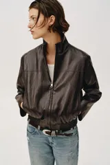 Chaqueta estilo bomber corta de efecto piel en color marrón oscuro, con cuello subido, cierre frontal con cremallera y cintura elástica fruncida.
