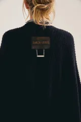 Poncho de punto grueso y sin mangas, color marrón tostado, abierto como capa y con ruedo asimétrico.
