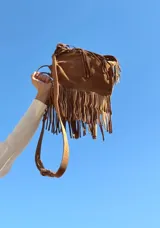 Cartera de gamuza color marrón con diseño de flecos largos en toda la superficie. Cuenta con asas cortas y una correa larga ajustable y extraíble para usar como bandolera.