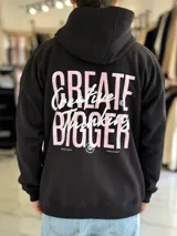 Canguro oversize de color beige claro con capucha, mangas largas y puños elastizados. Presenta un diseño gráfico en la espalda con el texto 'Creative Thinking' en tipografía cursiva negra sobre un fondo de letras grandes en tono rosado.
