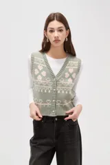 Chaleco tejido de punto con diseño jacquard de corazones y motivos geométricos en tonos verde y rosa. Presenta escote en V, cierre frontal con botones y terminaciones acanaladas en cuello, sisas y ruedo.