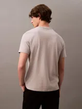 Remera gris claro de algodón con cuello redondo y manga corta. Presenta un estampado tonal con el logo de Calvin Klein Jeans en el pecho.