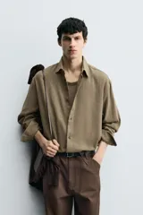 Camisa de manga larga color marrón verdoso, con cuello solapa y cierre frontal de botonadura. Presenta un tejido con textura rústica y un calce relajado.