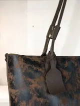 Cartera tipo tote de gran tamaño, confeccionada en cuero genuino con acabado texturizado y efecto desgastado en tonos tierra y negro. Cuenta con cierre superior metálico, interior forrado en cuero y un sujetador de asas con broche decorativo.