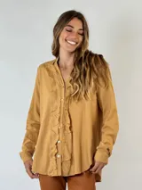 Camisa color mostaza con volados desflecados a lo largo de la botonadura frontal, cuello mao y mangas largas con puños abotonados.