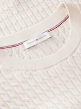 Sweater de punto trenzado fino de color blanco, confeccionado en puro algodón, con cuello redondo y mangas cortas. Presenta un pequeño logo bordado en el pecho.