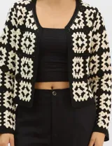 Cardigan abierto de tejido de punto calado con diseño geométrico bicolor en mangas y paneles frontales, y espalda en tono sólido. Presenta silueta recta, frente abierto sin cierre y terminaciones con vivos reforzados en escote, puños y ruedo.