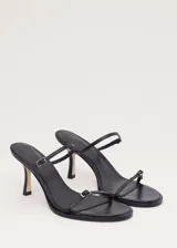 Sandalias de tacón alto color negro, con diseño minimalista de tiras finas cruzadas en el empeine y cierre con hebilla en el tobillo.