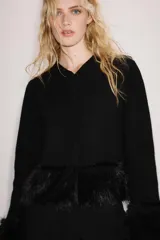 Chaqueta de punto negra con cuello redondo y manga larga, con detalles de pelo sintético a tono en los puños y en el bajo. Cuenta con cierre frontal con botones a presión ocultos.