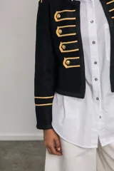 Chaqueta corta negra de paño con corte entallado, detalles dorados bordados, botones metálicos y cuello redondo.