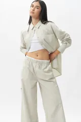 Pantalón de corte amplio y estilo piyamero, confeccionado en algodón con estampado de rayas verticales finas en color verde y blanco. Cuenta con cintura elástica y múltiples bolsillos laterales.