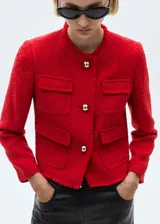 Chaqueta de tweed color rojo con cuello redondo, manga larga y diseño corto. Presenta cuatro bolsillos de parche en la parte frontal, cierre de botones metálicos y terminaciones deshilachadas.