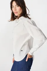 Camisa de color marrón claro, con cuello clásico, cierre frontal de botones y mangas largas con puños ajustados y volumen en los hombros.