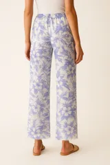 Pantalón de algodón color beige con estampado de hojas tropicales en tonos más oscuros de beige. Tiene cintura elástica, corte ancho y calce alto, con bolsillos laterales y terminación deshilachada en los tobillos.