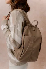 Mochila color tostado con compartimento principal con cierre, bolsillo frontal con cierre oculto, bolsillos laterales y asa superior. Cuenta con logo metálico de la marca Peach.
