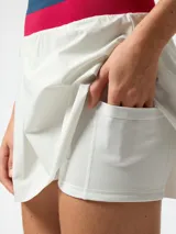 Skort deportivo blanco con pretina ancha tejida en colores fucsia y azul. Cuenta con short incorporado en el interior y diseño plisado central, inspirado en el estilo de tenis vintage.
