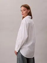 Camisa blanca de algodón con cuello camisero, manga larga y cierre frontal con botones. Presenta un sutil estampado integral de logo de Calvin Klein.