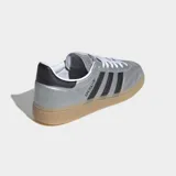 Championes Adidas Handball Spezial de caña baja, con exterior de cuero sintético metalizado color plata y tres franjas laterales negras. Presentan detalles en negro en el talón y cuello, cordones blancos y suela de caucho color caramelo.