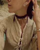 Gargantilla tipo choker de gamuza con dijes colgantes artesanales de metal y perlas naturales. Cuenta con tiras largas para atar y ajustar en la parte posterior.