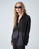 Camisa negra combinada bicolor confeccionada en telas italianas, de silueta holgada. Tiene cuello camisero, cartera con botones, y un bolsillo plaqué. Las mangas largas presentan pliegues en los puños y tablitas en la espalda.