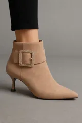 Botín de gamuza color beige con punta fina y tacón kitten. Presenta una correa con hebilla cuadrada con incrustaciones de strass alrededor del tobillo.