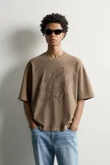 Remera relaxed fit color marrón con cuello redondo, manga corta y parche bordado a tono con letras en el frente.