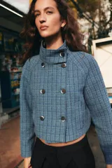 Chaqueta corta de cuello subido y manga larga, con diseño de cuadros en tonos azules. Presenta cierre frontal cruzado con botones oscuros y bolsillos de vivo en el delantero.