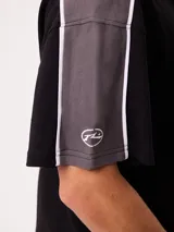 Remera polo gris melange de ajuste holgado, con cuello y cierre frontal de botones. Presenta detalles en azul marino y blanco en los hombros y mangas, y el logo de la marca bordado en el pecho.