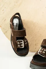 Sandalias negras de cuero con diseño de plataforma dentada, tiras ajustables con hebillas metálicas y detalle de tachas plateadas en el lateral de la suela.