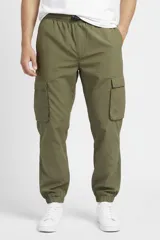Pantalón cargo de nylon color verde militar, con cintura elástica y cordón ajustable, bolsillos laterales tipo cargo con solapa y puños elásticos en los tobillos.