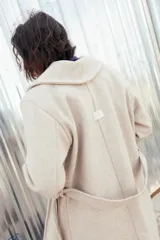 Tapado largo de paño color beige, con solapa amplia, mangas largas y cinturón ajustable para anudar en la cintura.