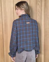 Camisa de manga larga con estampado de cuadros en tonos azules y rojizos. Presenta un cuello alto con volados y puños elásticos con detalle de volado en el extremo. Cierre frontal con botones ocultos.